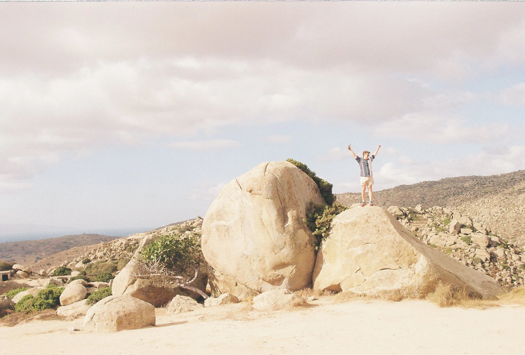 A person standing on a large rock in a desert landscape with mountains in the background, raising their arms in celebration.