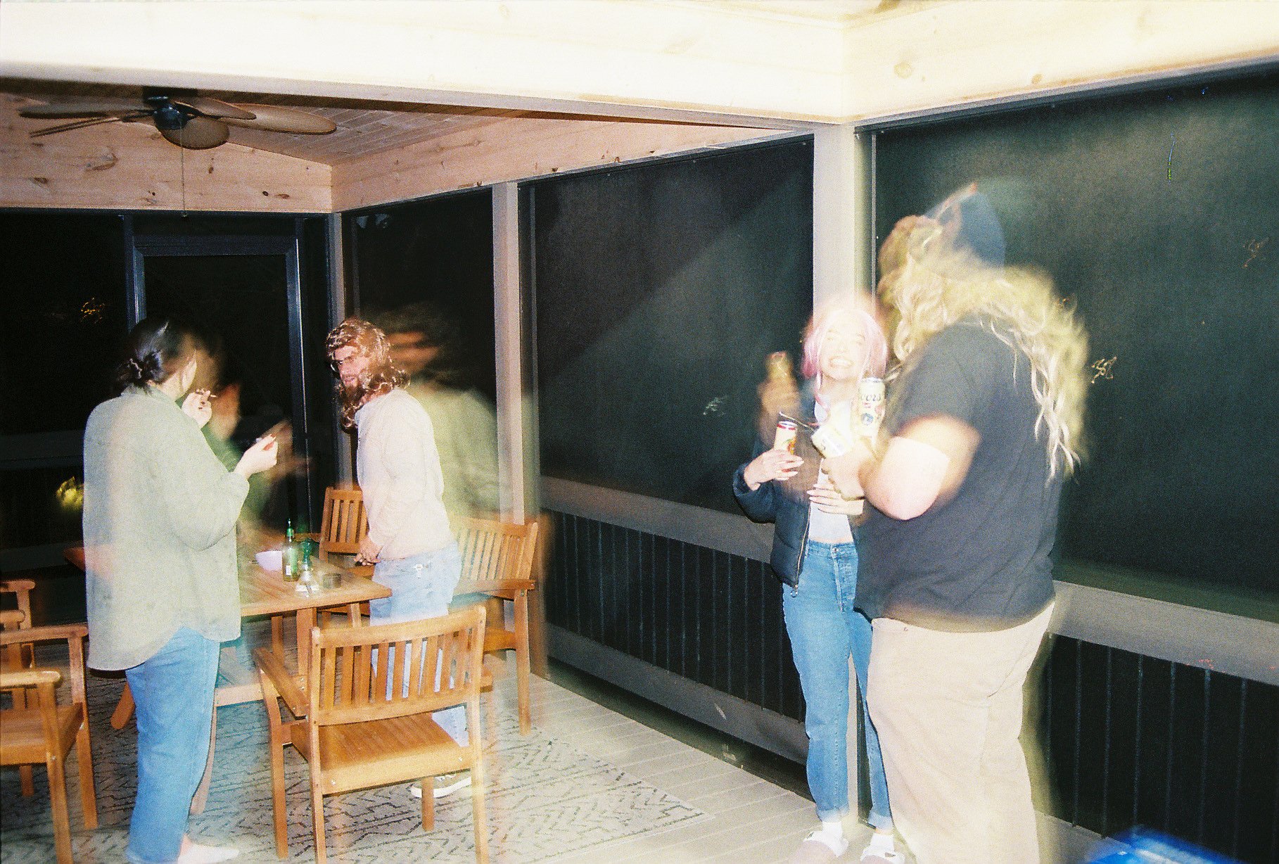 Four women socializing indoors at night, one with short hair and another with long blonde hair, all holding drinks and chatting.