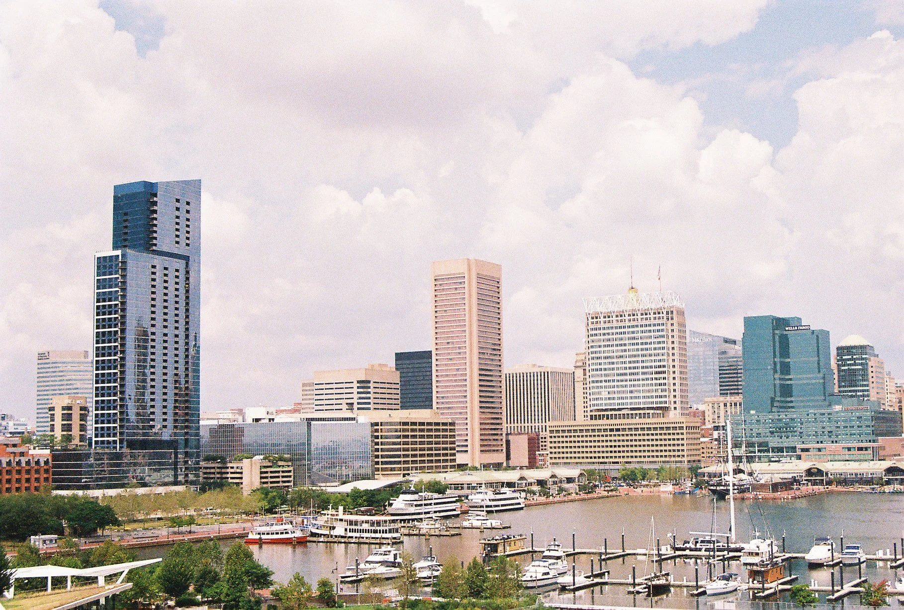 City skyline with high-rise buildings and a marina with boats in the foreground, under a partly cloudy sky.