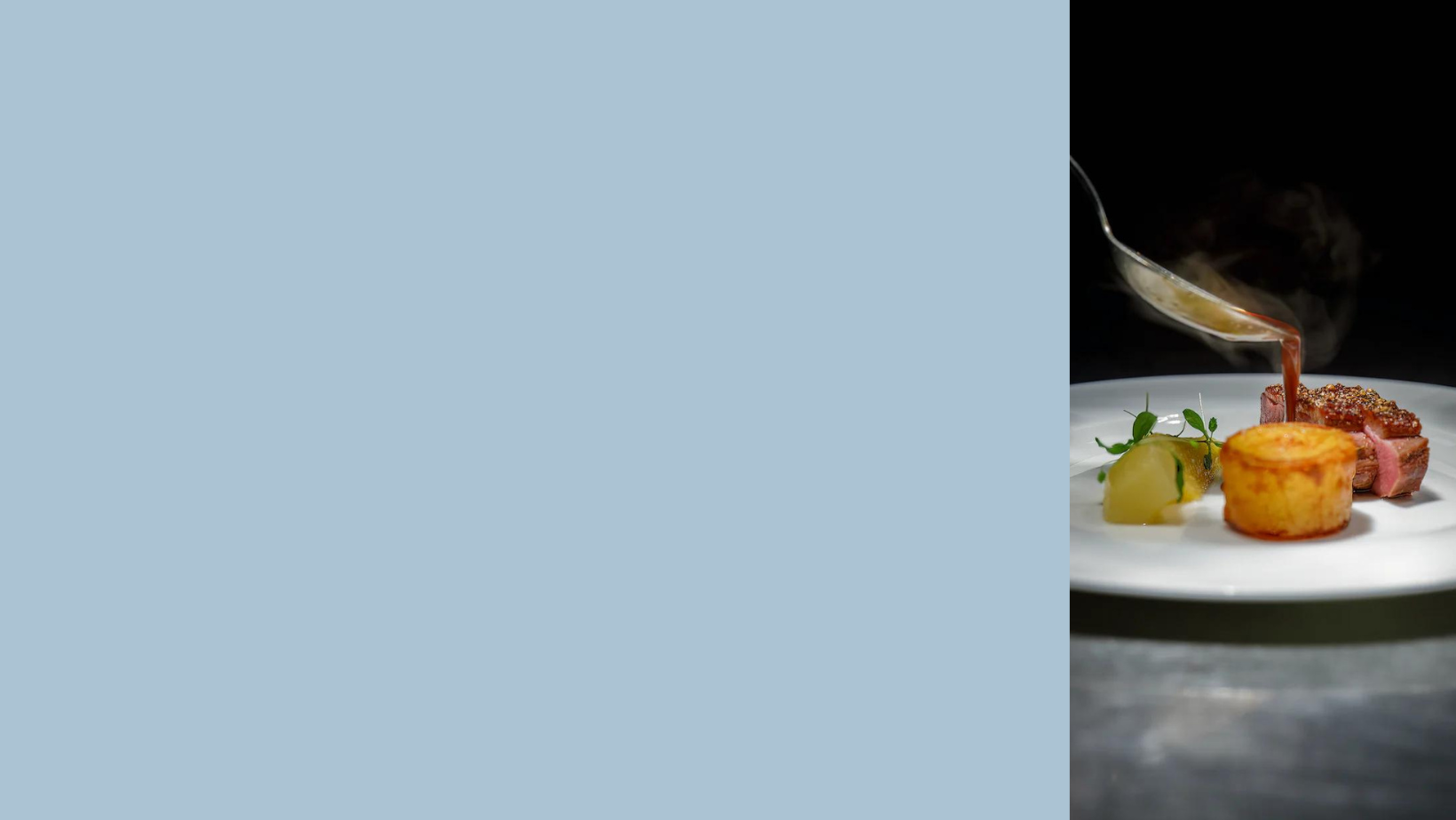 Blue background with person spooning the final touch of sauce onto fondant potato beside some tender roasted duck breast. 