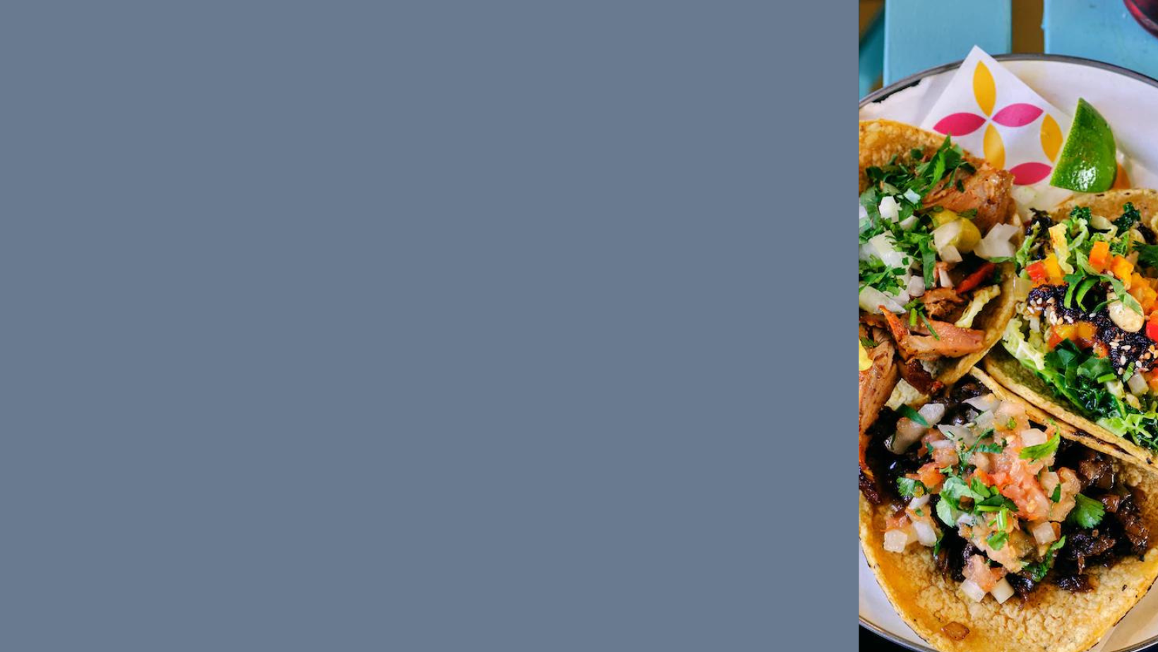 three tacos on a napkin on a plate on a blue picnic table. The tacos are fresh corn crunchy and fresh and filled with local Mexican ingredients like Al pastor