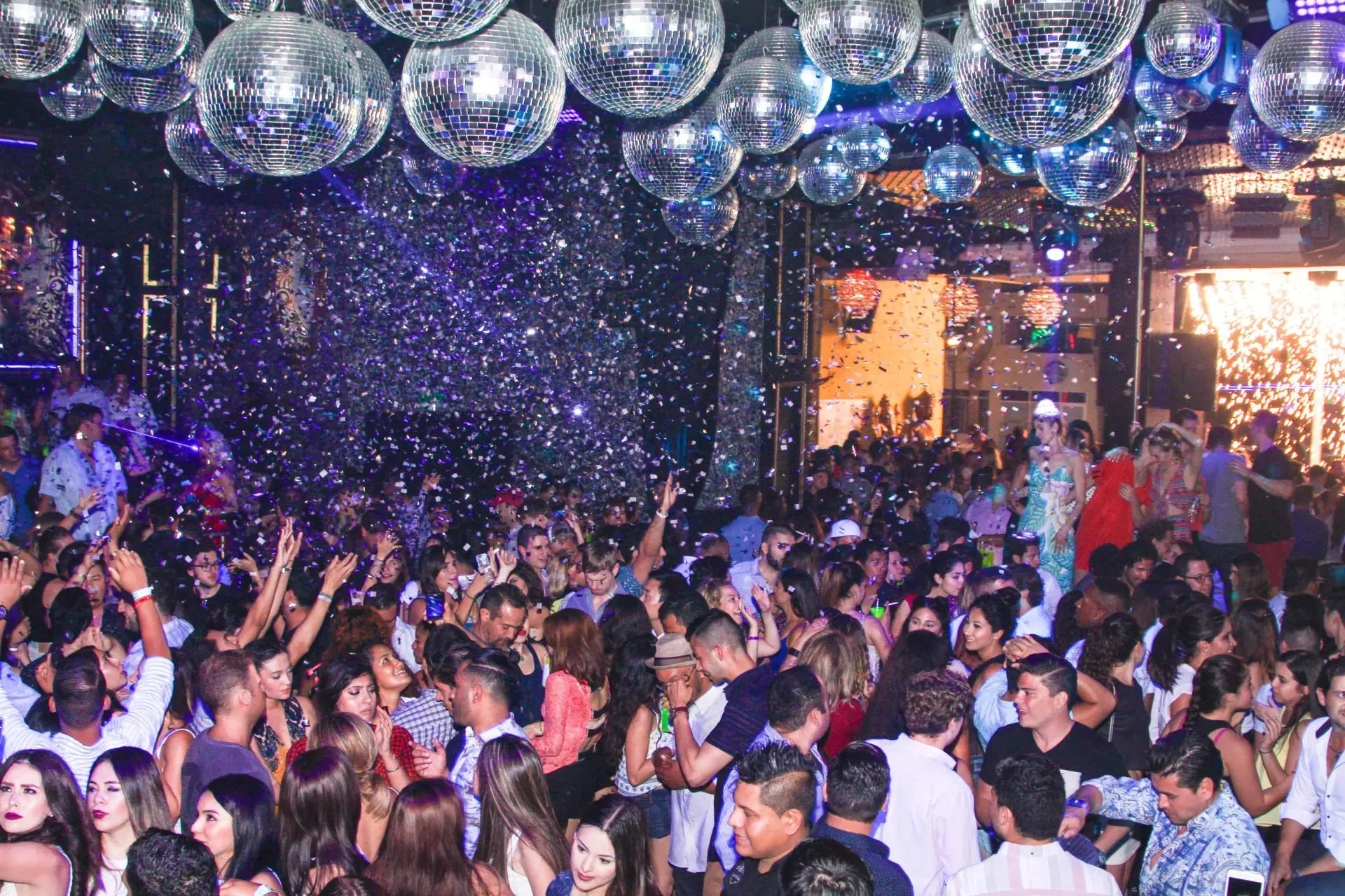 A photo of the packed dance floor at Mandala night club in Cabo San Lucas. There is glitter in the air and the ceiling is filled with shining disco balls. Party goers look like they are having a great time with their hands in the air. Vacation Rental