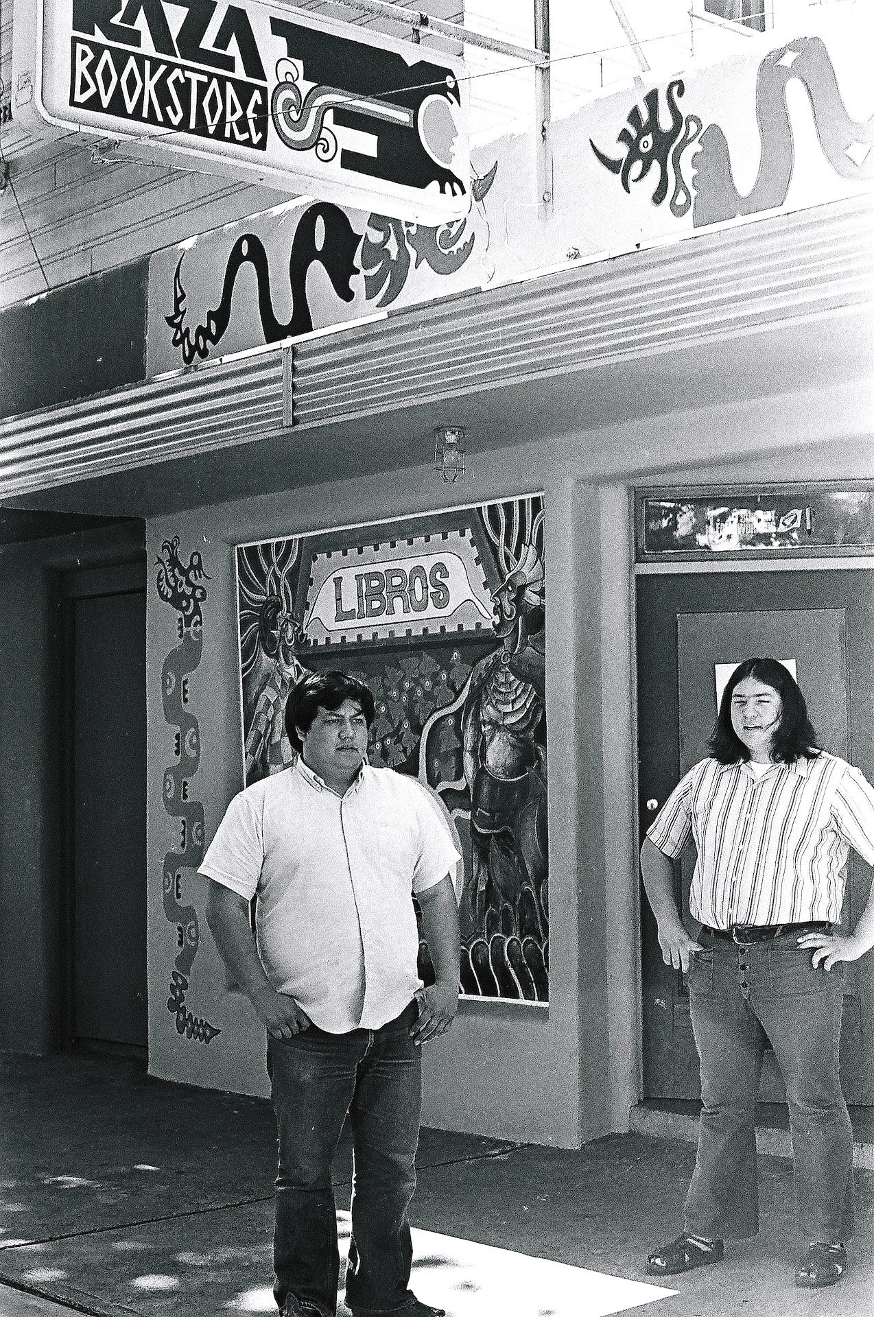 Two men standing outside a bookstore with colorful street art and signs.
