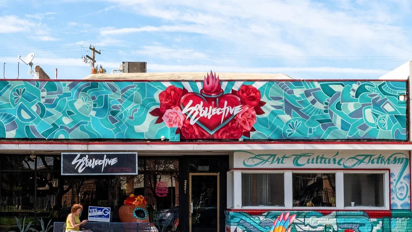 The storefront of an art gallery with colorful wall murals, including a large heart with roses and flames, and a sign reading 'Art Culture Activism'.