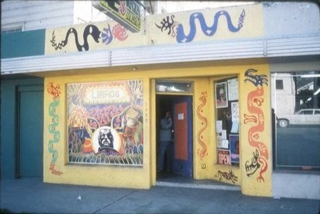 Street view of a colorful bookstore with yellow walls and painted snakes, with a person standing in the doorway.
