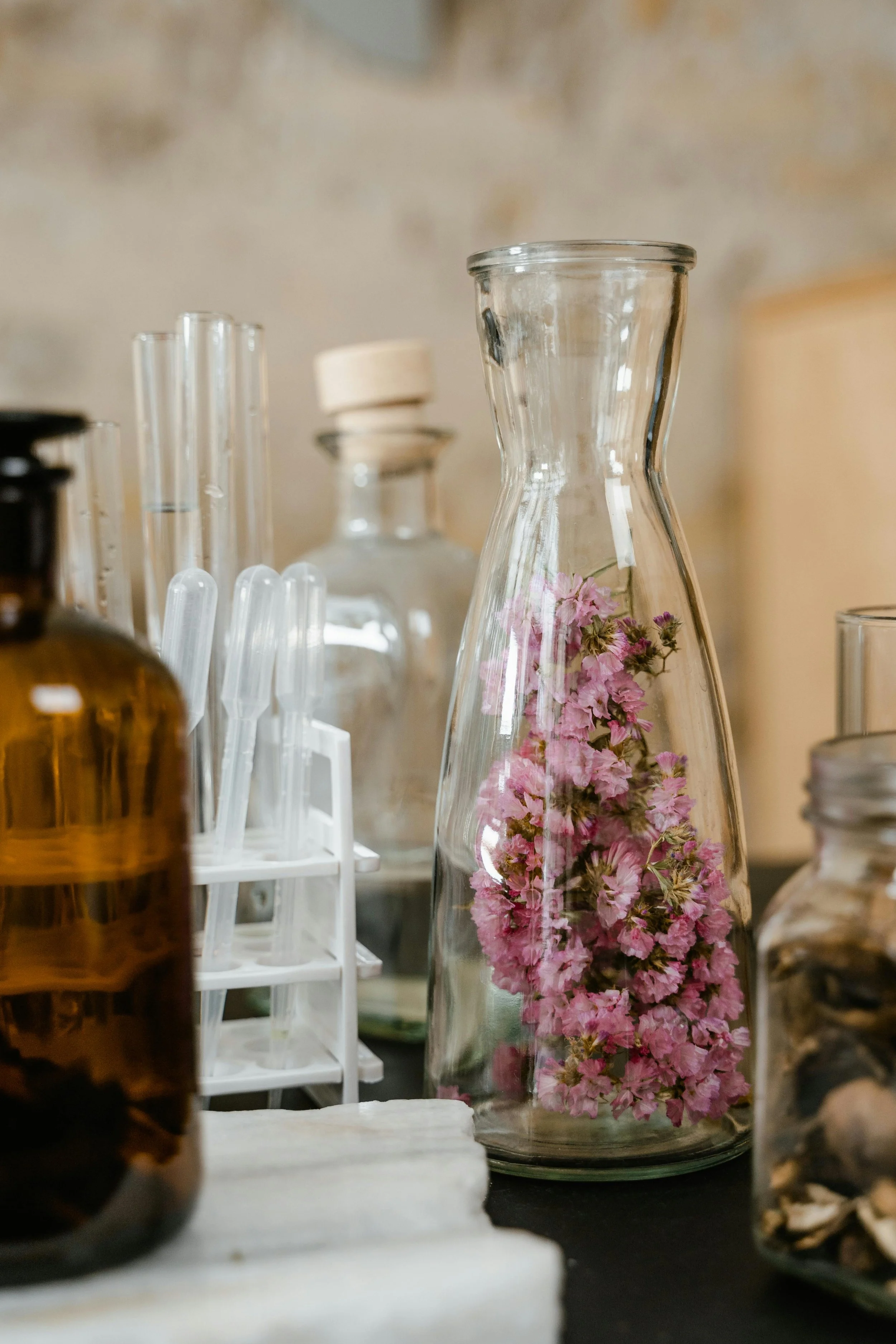 A glass vase with pink flowers inside, surrounded by various bottles and laboratory glassware, on a table.