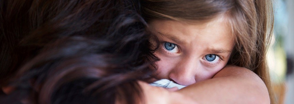 Close-up of a young girl with blue eyes hugging someone with dark hair, showing emotion.