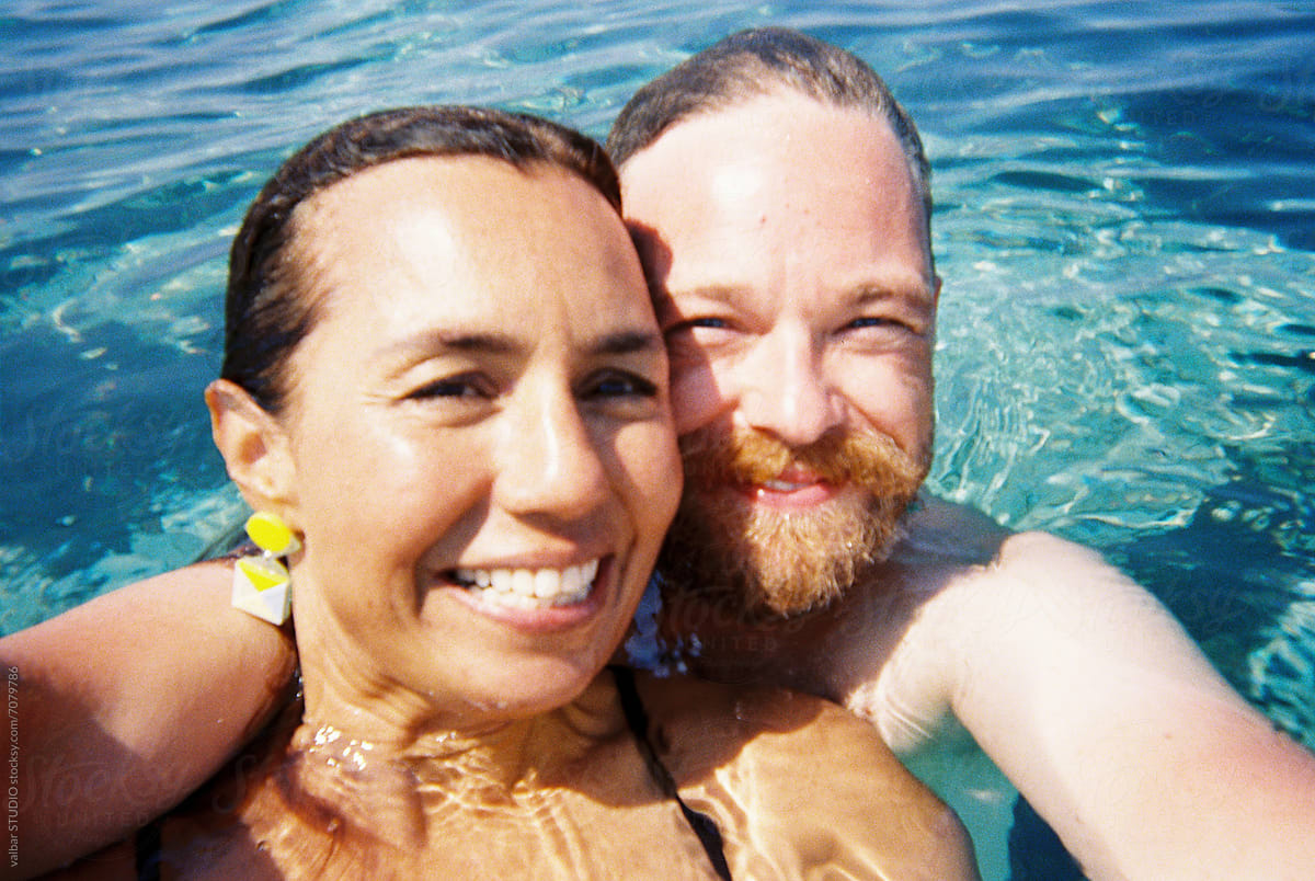 A smiling woman and man taking a selfie in a swimming pool.