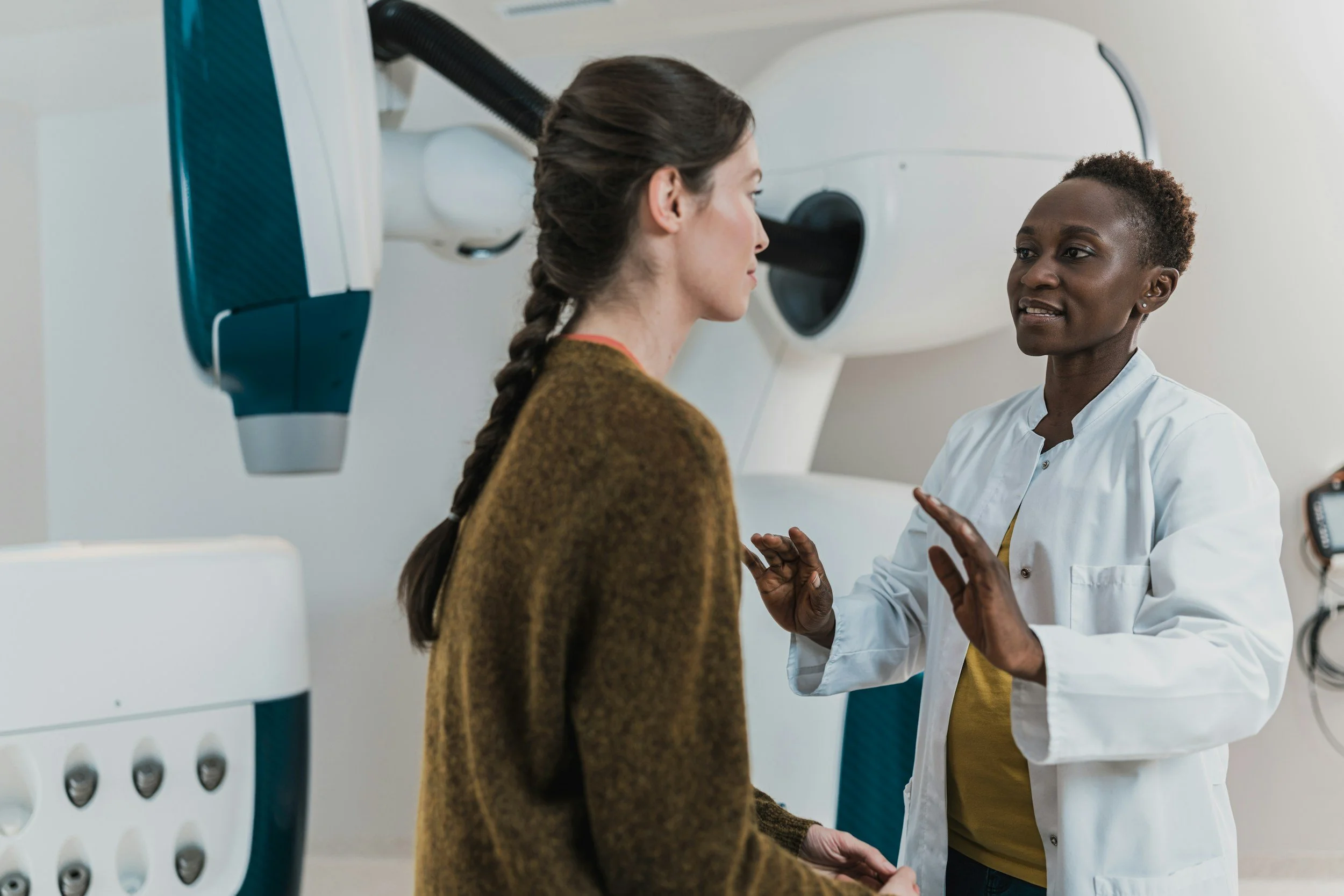 Medical professional explaining medical procedure to a female patient in a clinic with medical equipment in the background.