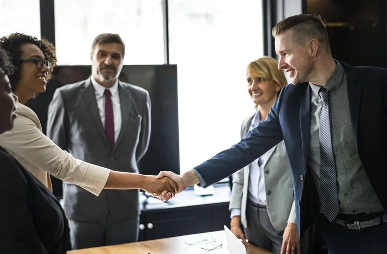 Businesspeople in a meeting handshake in a modern office.