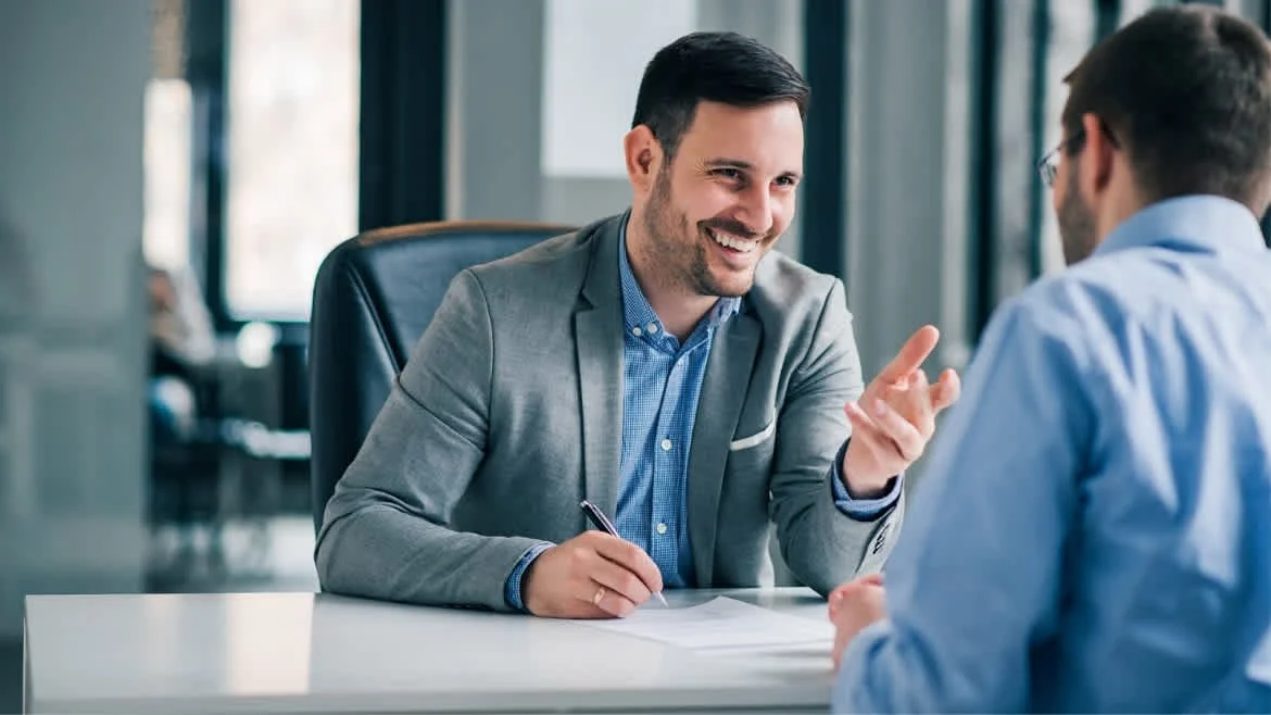 Two men having a business meeting in an office, smiling and engaged in a conversation.