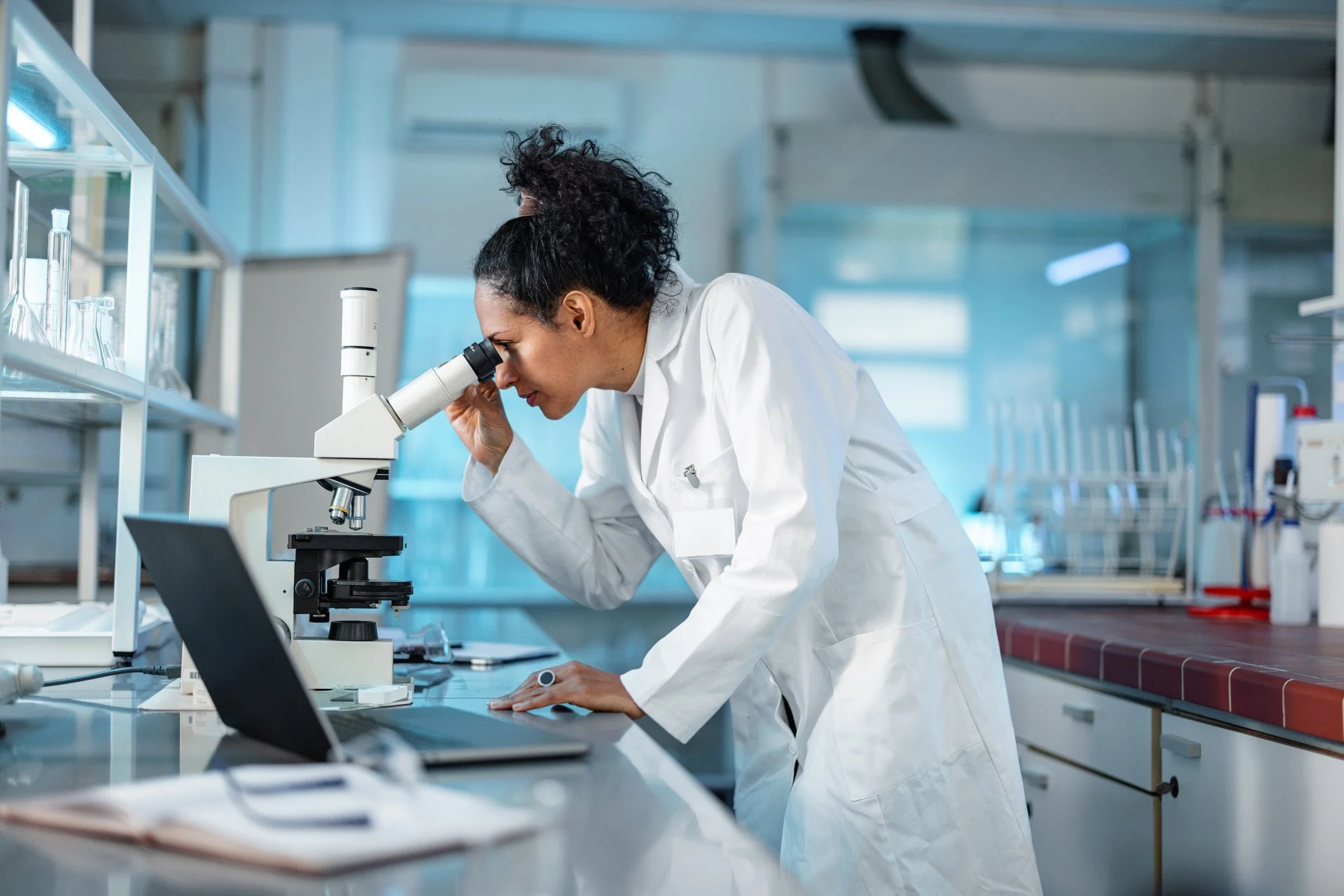 Female scientist in a white lab coat looking through a microscope in a laboratory.
