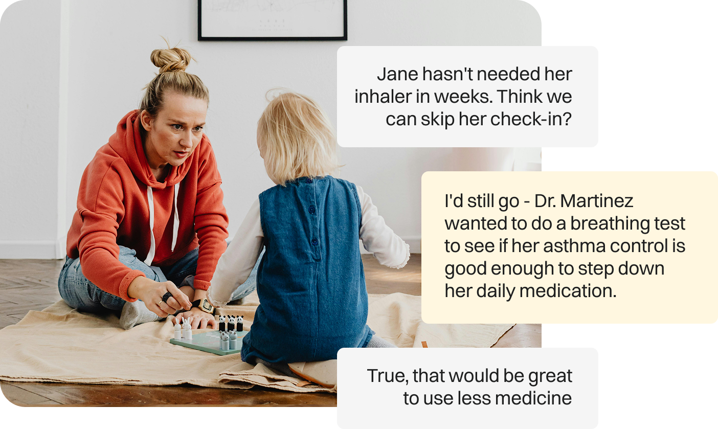 A woman with a bun hairstyle and wearing a rust-colored hoodie is sitting on the floor, playing a board game with a young girl with blonde hair wearing a blue vest and white long sleeve shirt. They are in a room with wooden flooring, a beige blanket, and a white wall with a black picture frame.