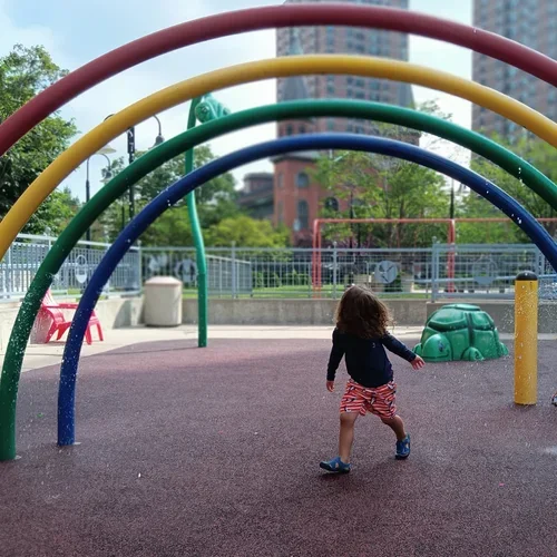 A young girl playing on a playground with colorful arches in a city park.