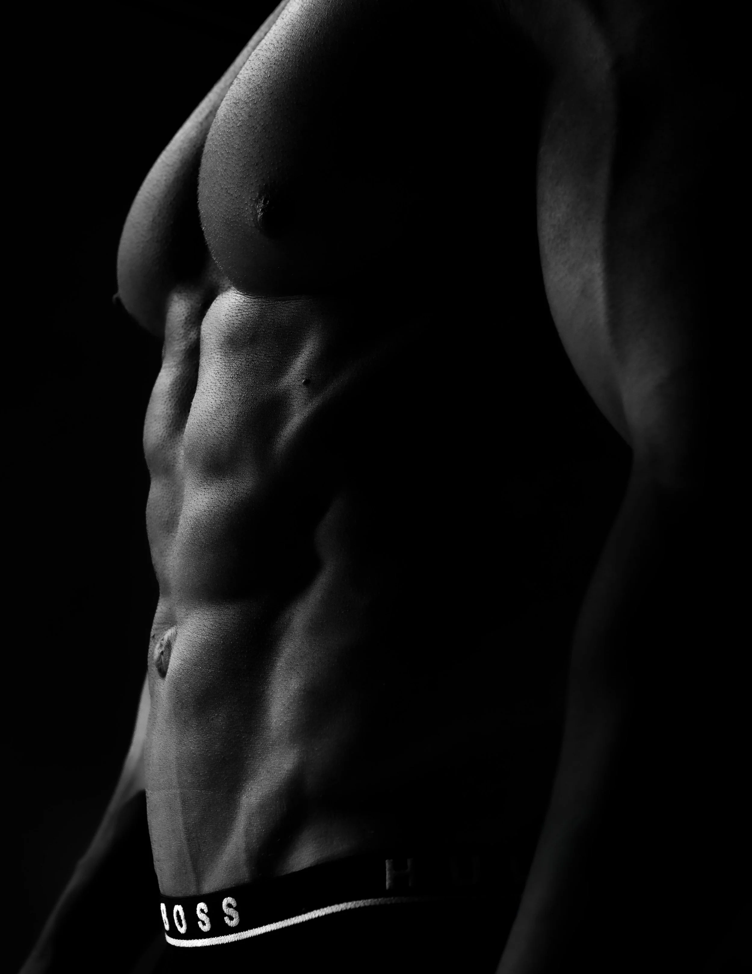 A black-and-white photograph of a male torso showing well-defined abdominal and chest muscles, with the focus on the muscular physique.