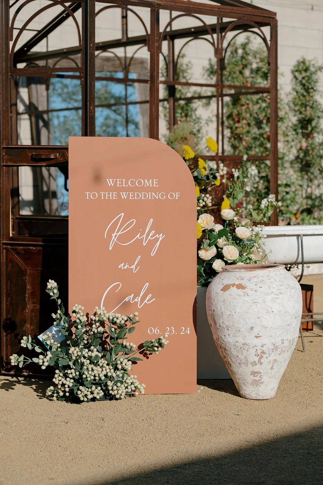 Wedding welcome sign with floral arrangements and a large urn.