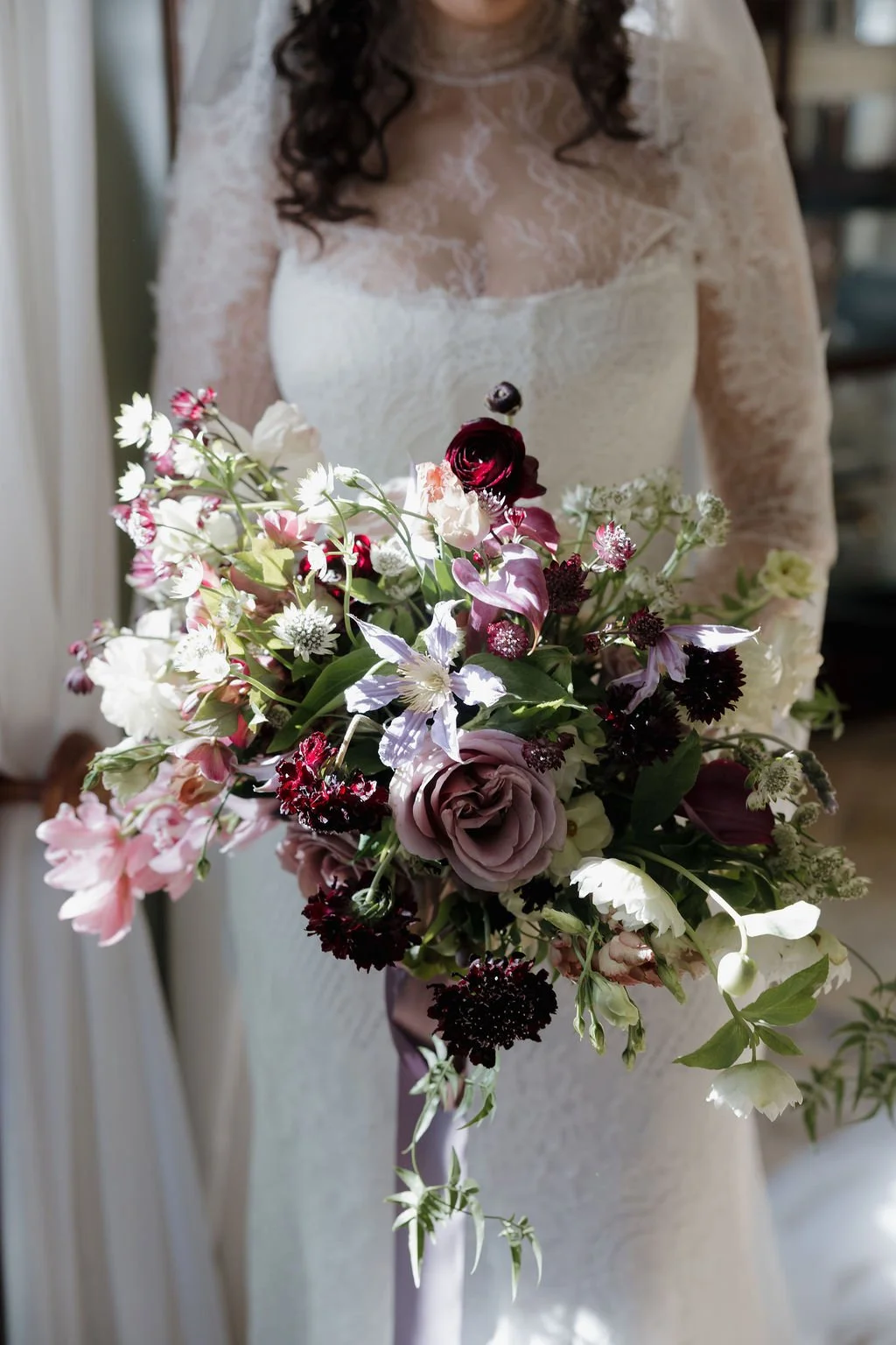 A woman in a lace dress holding a large bouquet of mixed flowers.