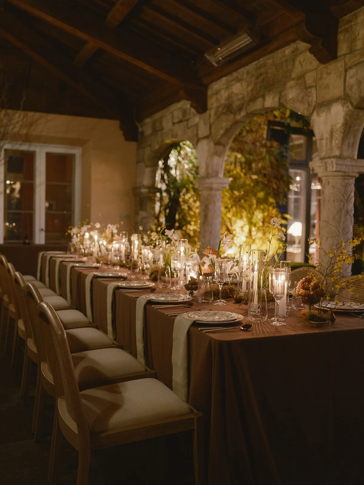 A long dining table set for a formal dinner with candles and floral centerpieces in a rustic, stone and wood interior.