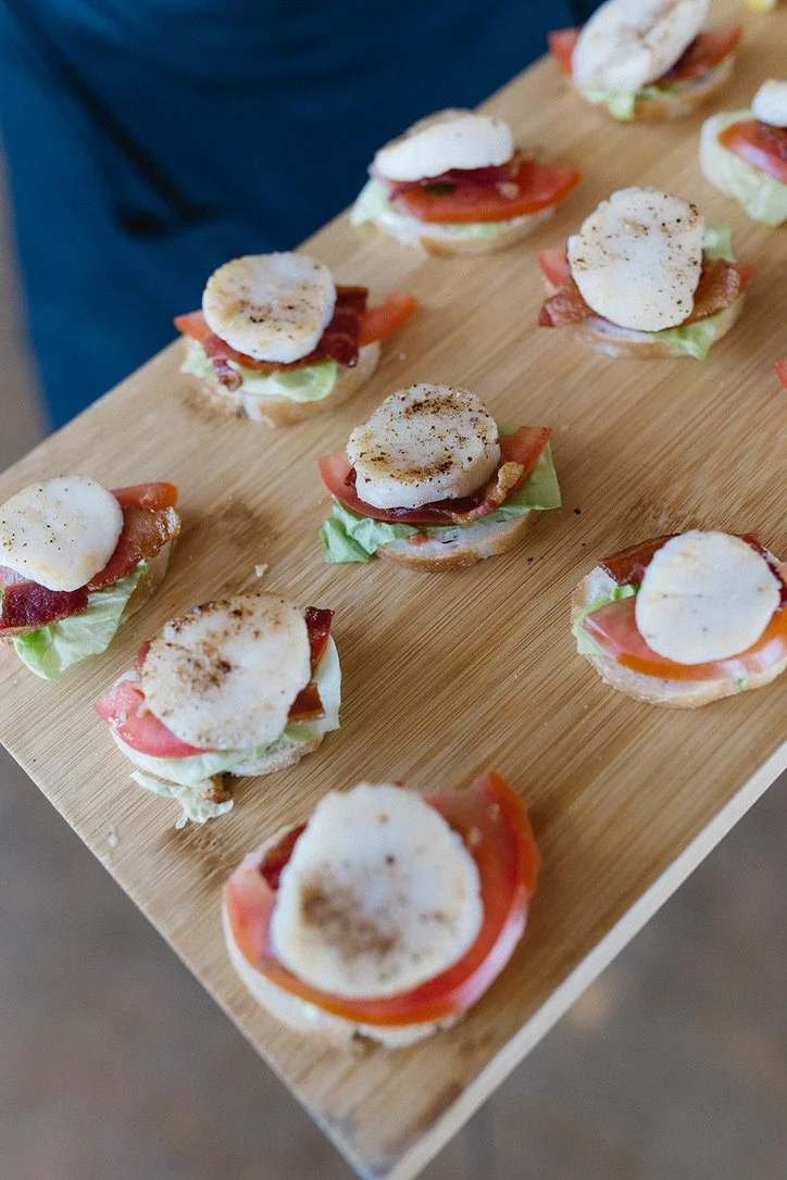 Miniature open-faced sandwiches with tomato, lettuce, bacon, and a poached egg, arranged on a wooden serving board.