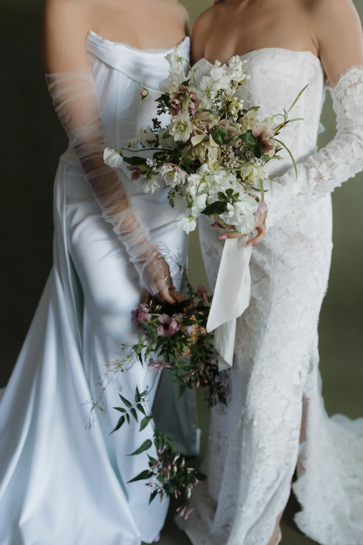 Two women in white wedding dresses holding bouquets of flowers, standing close together, with focus on their dresses and flowers.