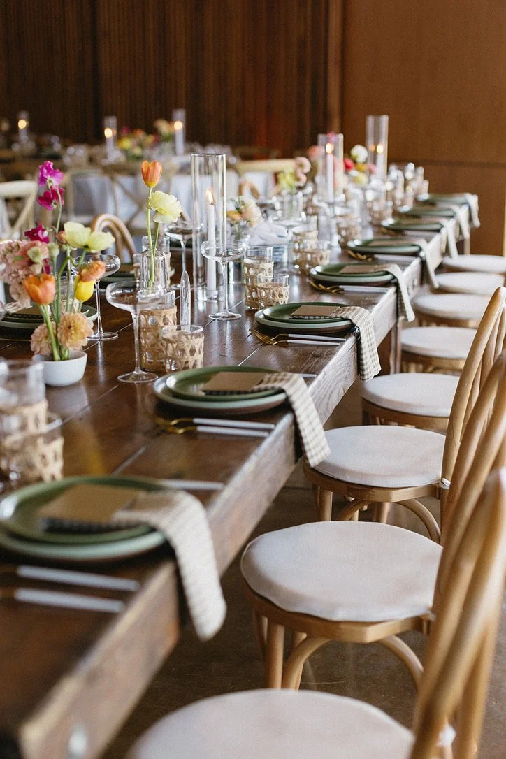 Elegant dining table set for an event or celebration with floral centerpieces, candles, glassware, and place settings.