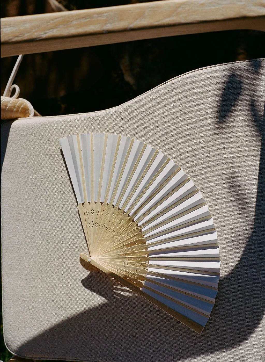 A hand fan resting on a beige fabric surface with a wooden edge in the background.