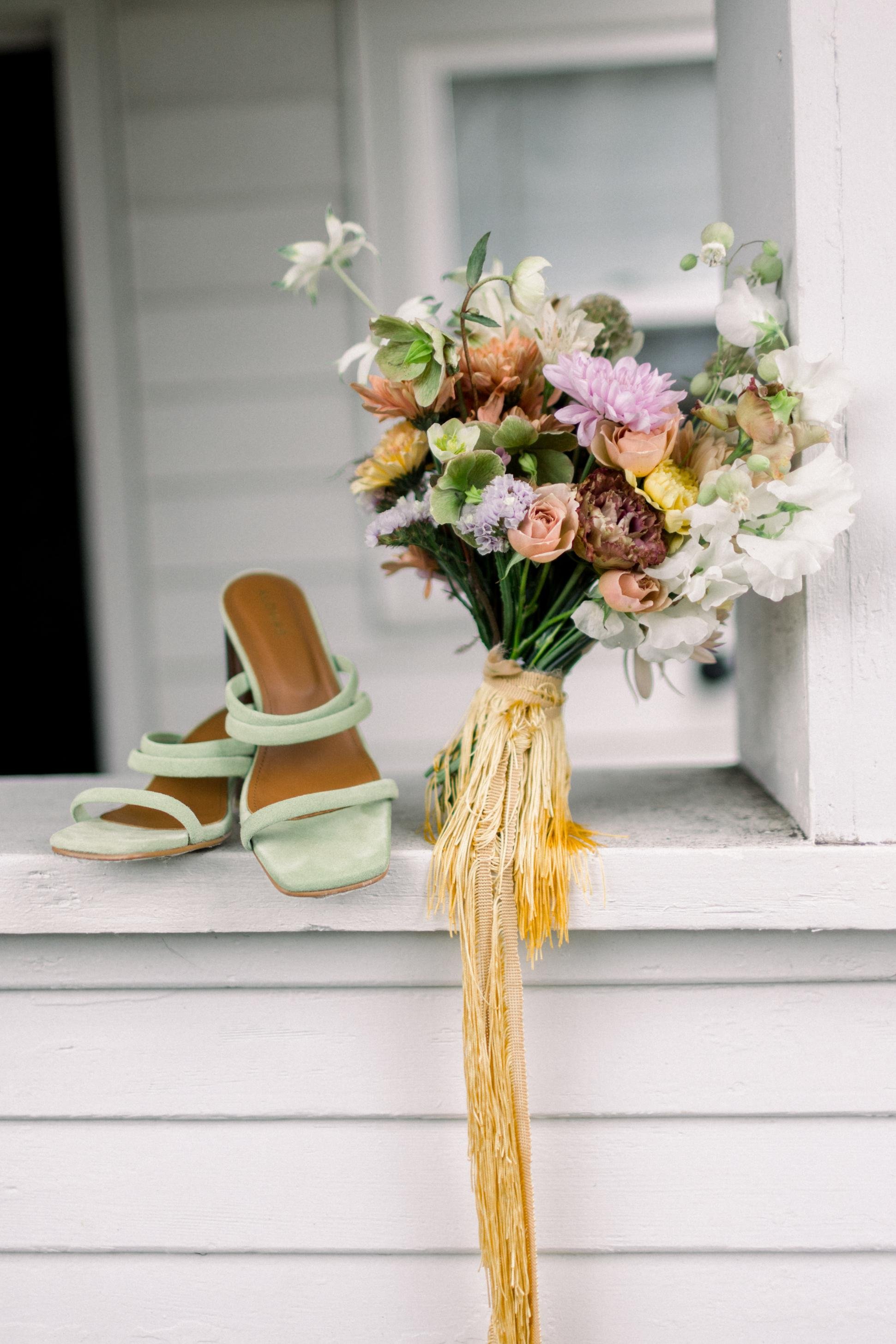 A pair of light green high-heeled sandals placed next to a bouquet of pastel-colored flowers in a yellow basket.