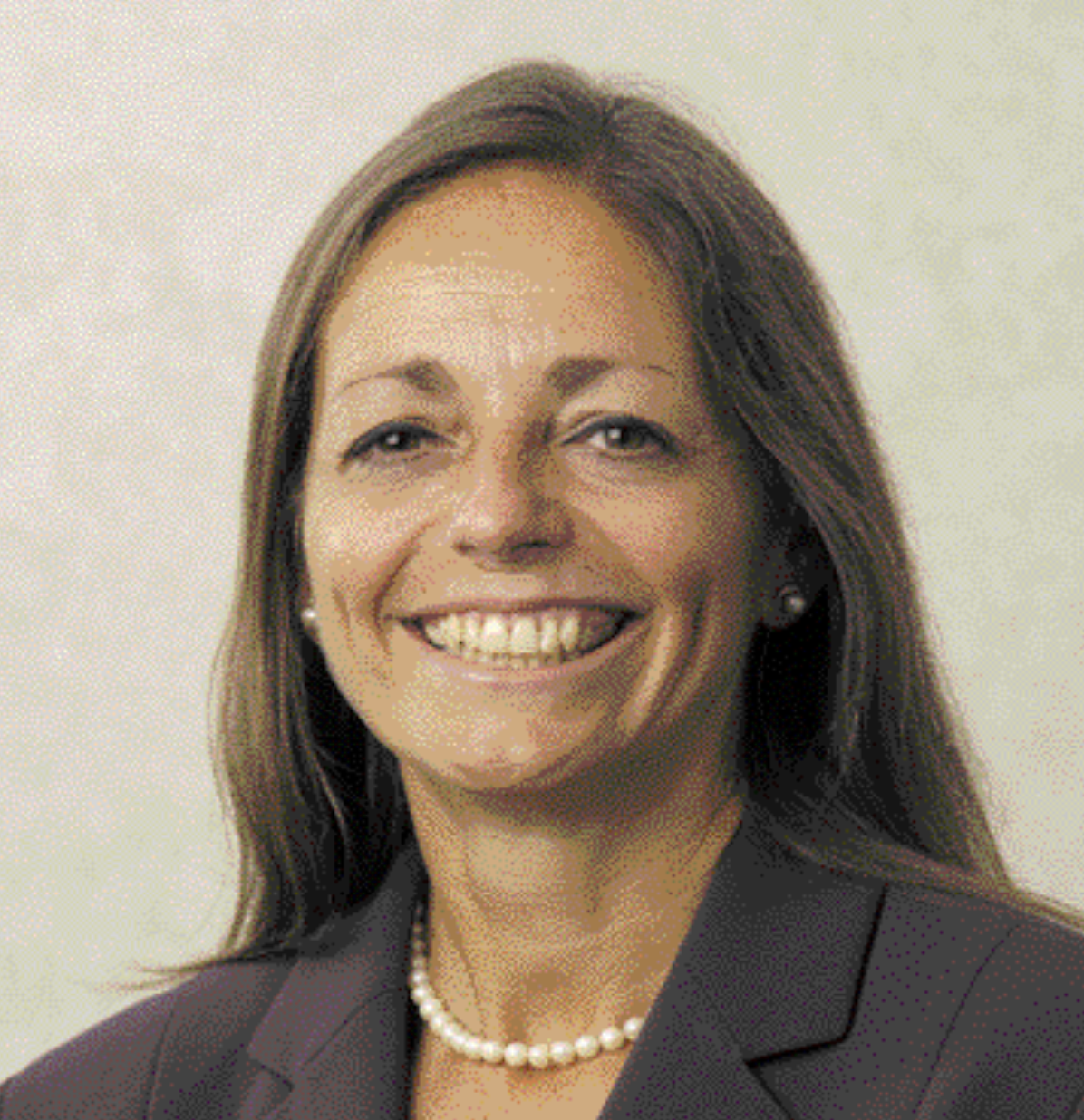 A smiling woman with shoulder-length brown hair wearing a dark blazer, pearl necklace, and pearl earrings.