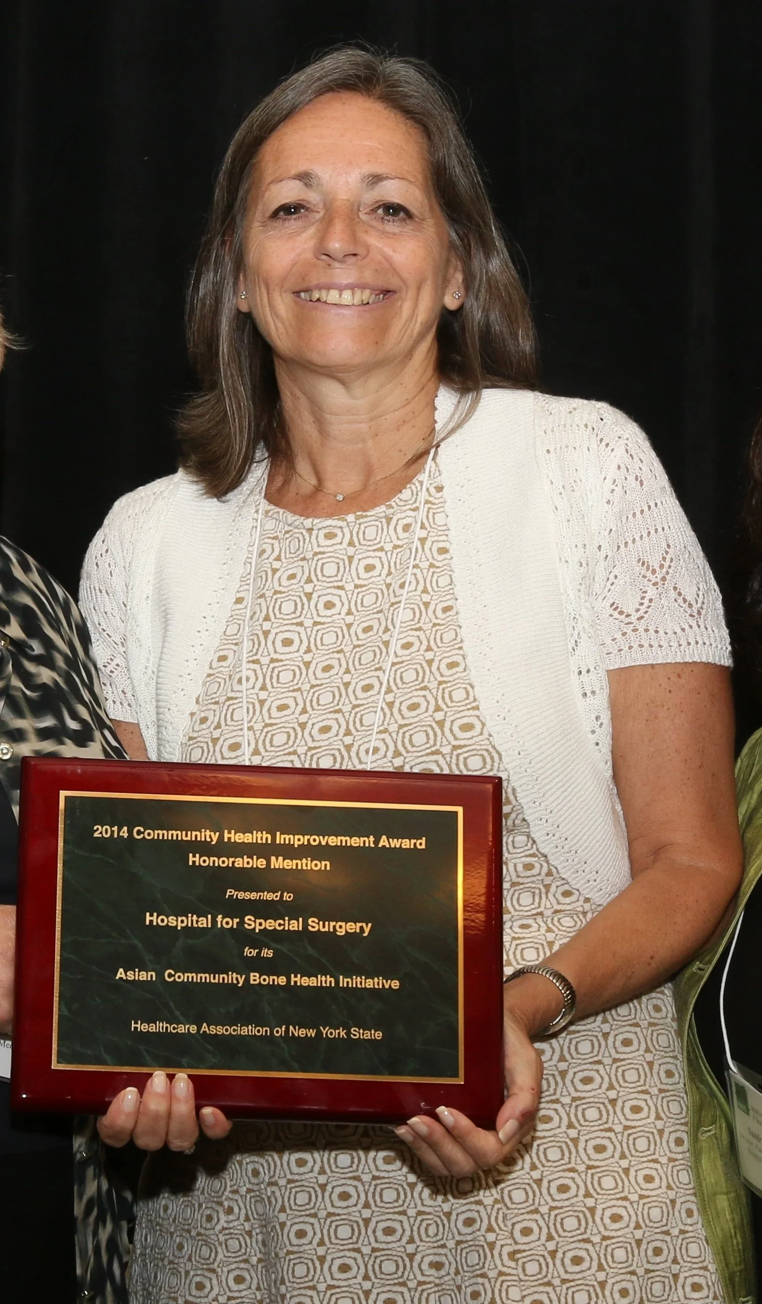 A woman with shoulder-length brown hair smiling and holding a plaque award.