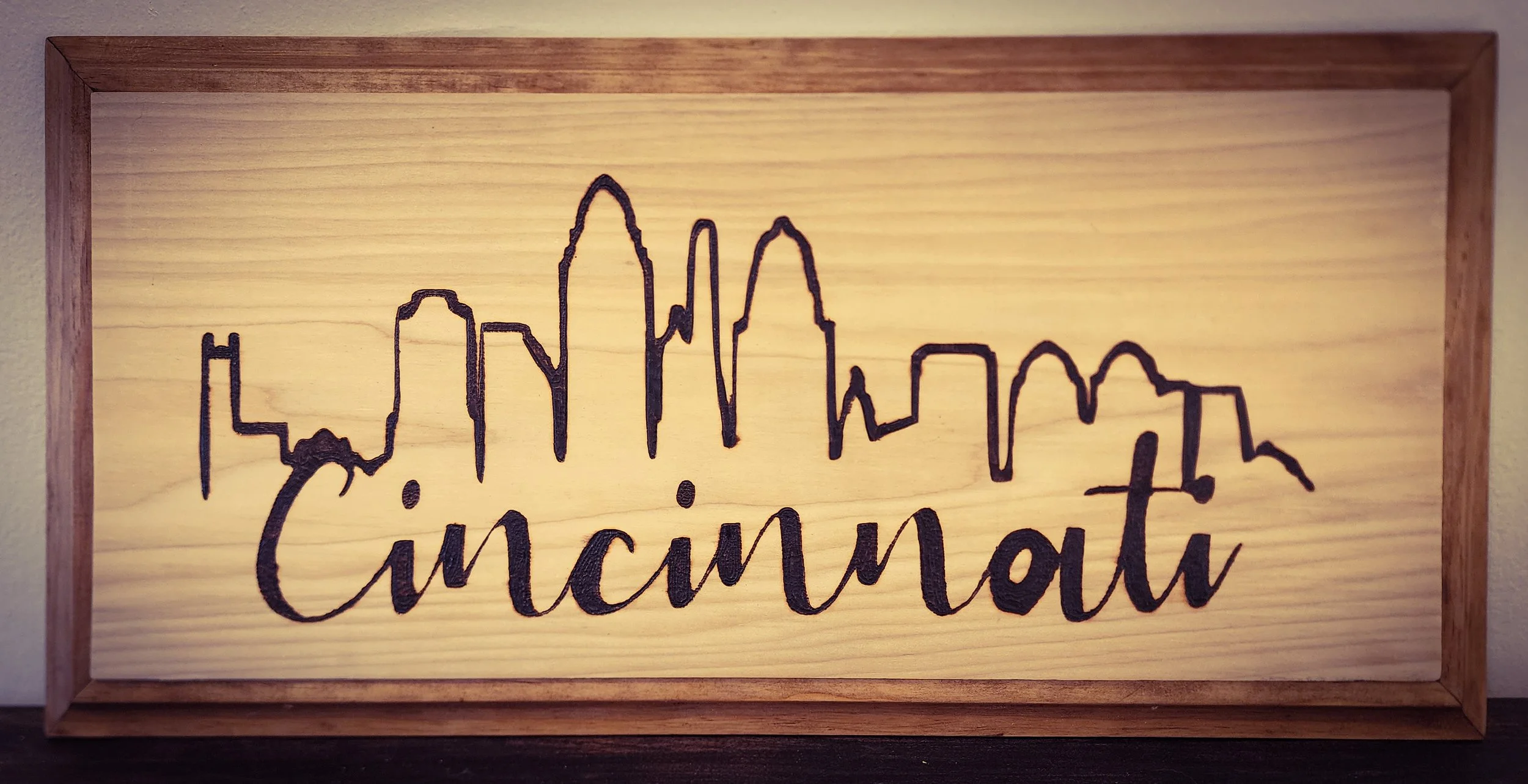 Wooden wall art with a black outline of Cincinnati's skyline and the word 'Cincinnati' written underneath.
