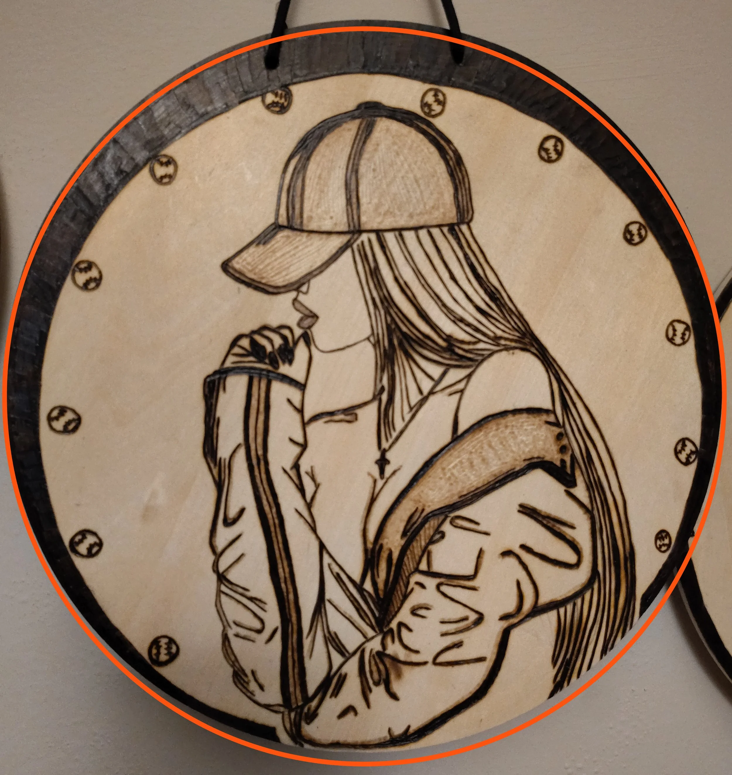A wood burnt sign with a drawing of a woman wearing a baseball cap and hoodie in a minimalist black and beige style.