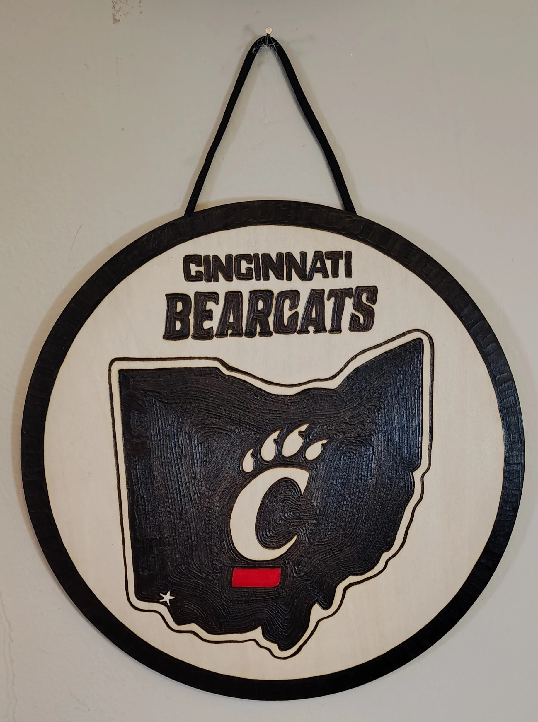 A circular wood burnt wall decoration with the text 'Cincinnati Bearcats' and an outline of the state of Ohio featuring a bearcat paw print and a red horizontal bar.
