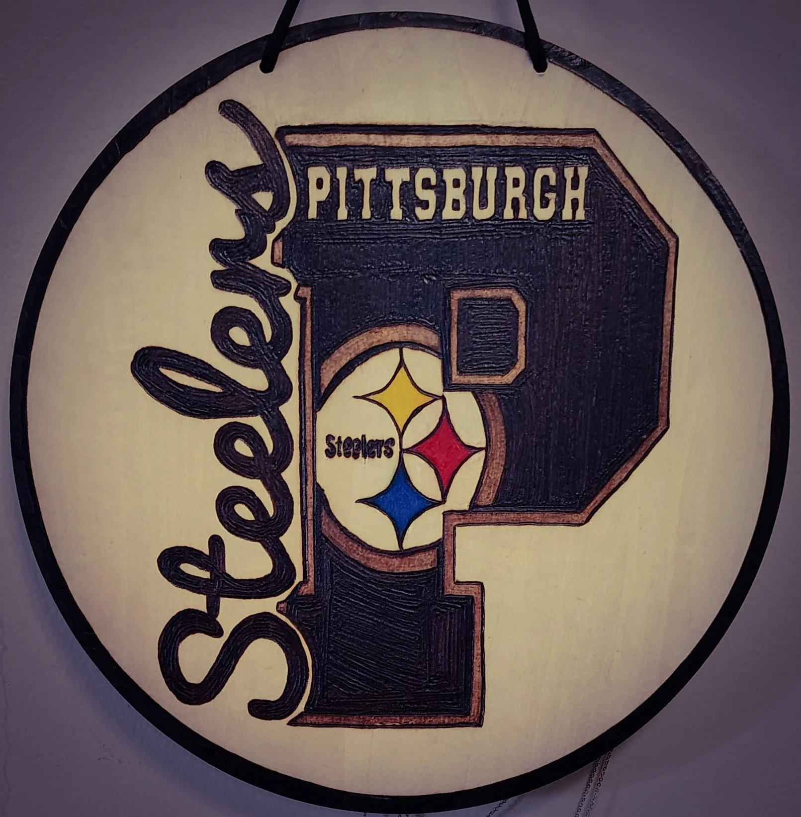 A round decorative wall hanging featuring the Pittsburgh Steelers football team logo with a large letter 'P' and the word 'Steelers' inside the letter, along with the team colors and the outline of the state of Pennsylvania.