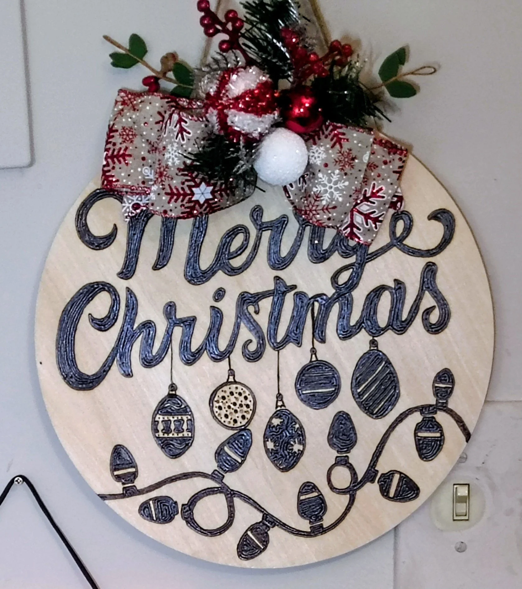Decorated wood burnt Christmas sign with the message "Merry Christmas" and hanging ornaments, adorned with a festive ribbon, red berries, and greenery.