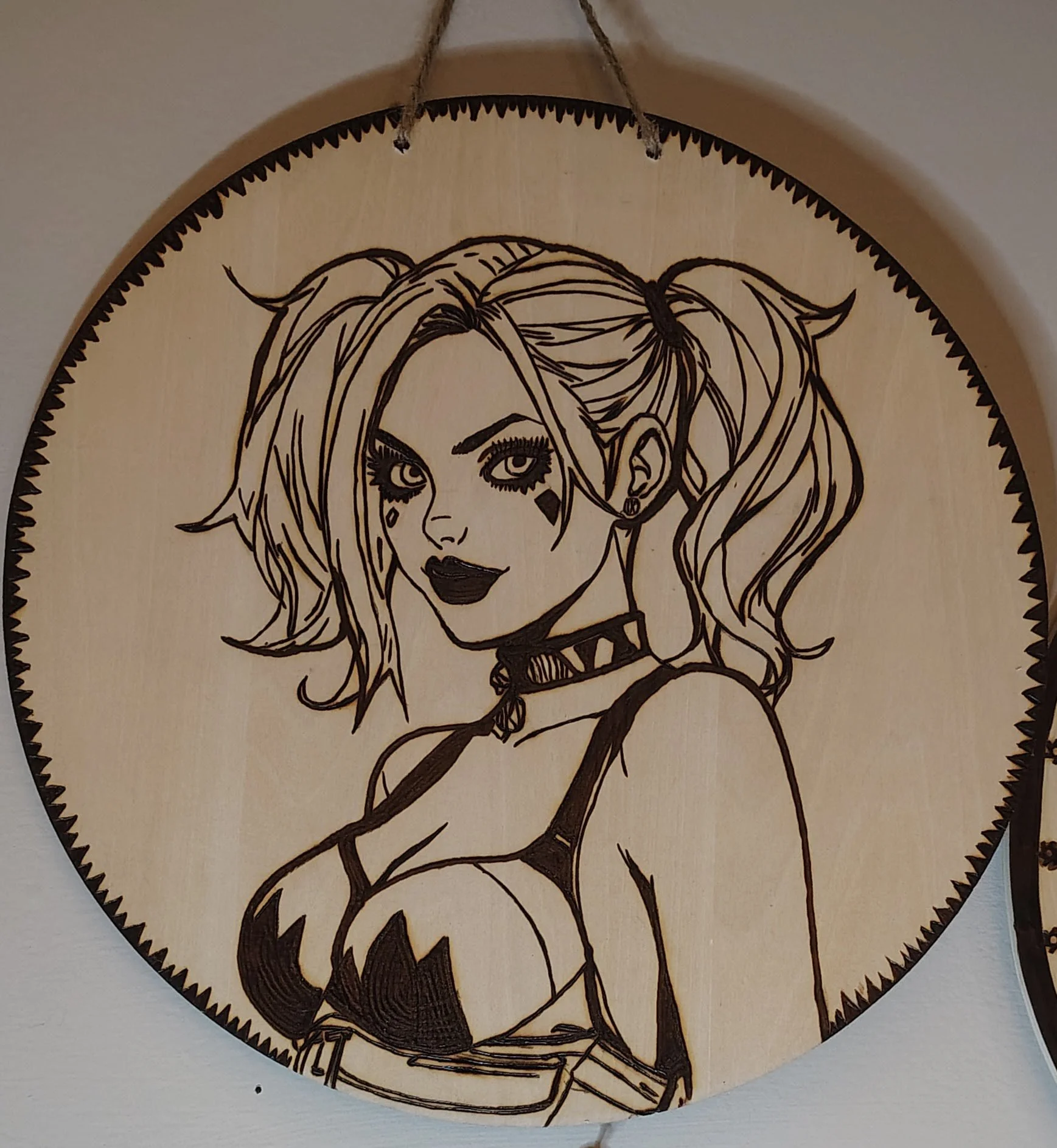 A round wooden wall hanging with a line art illustration of a woman with styled hair and makeup, wearing a choker and a revealing outfit, hanging from a string.