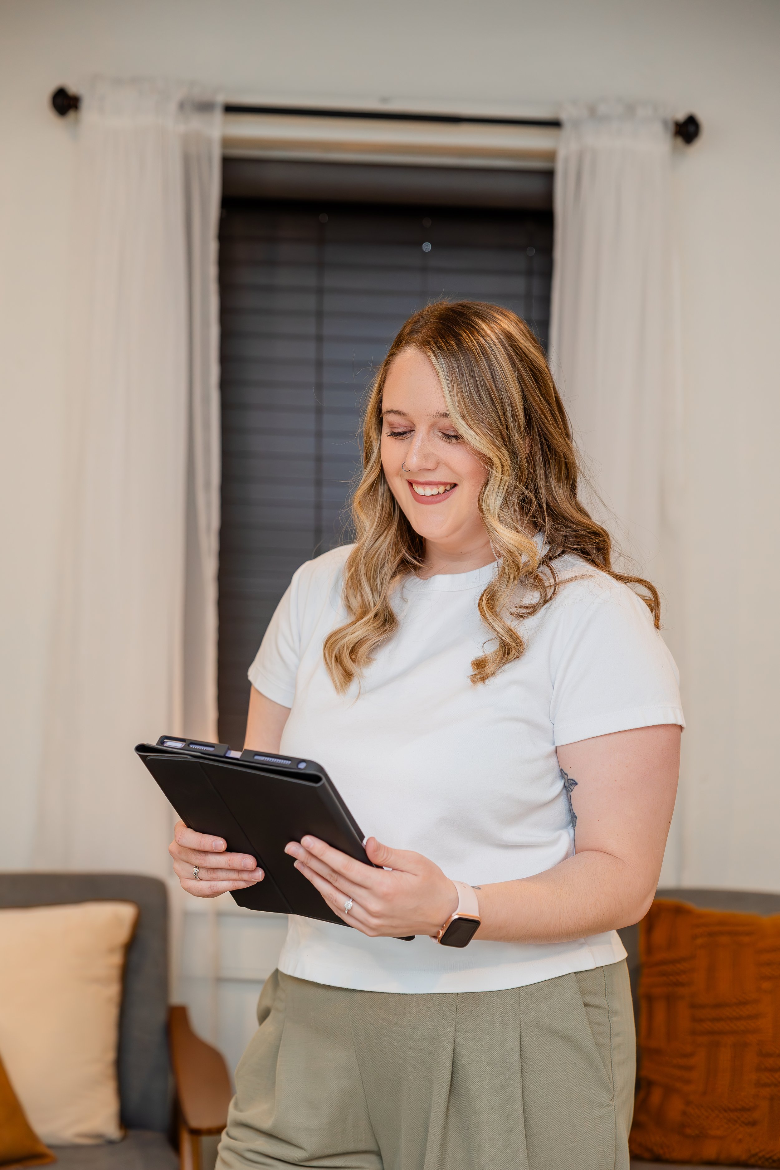 Smiling woman in casual clothes looking at tablet in living room.