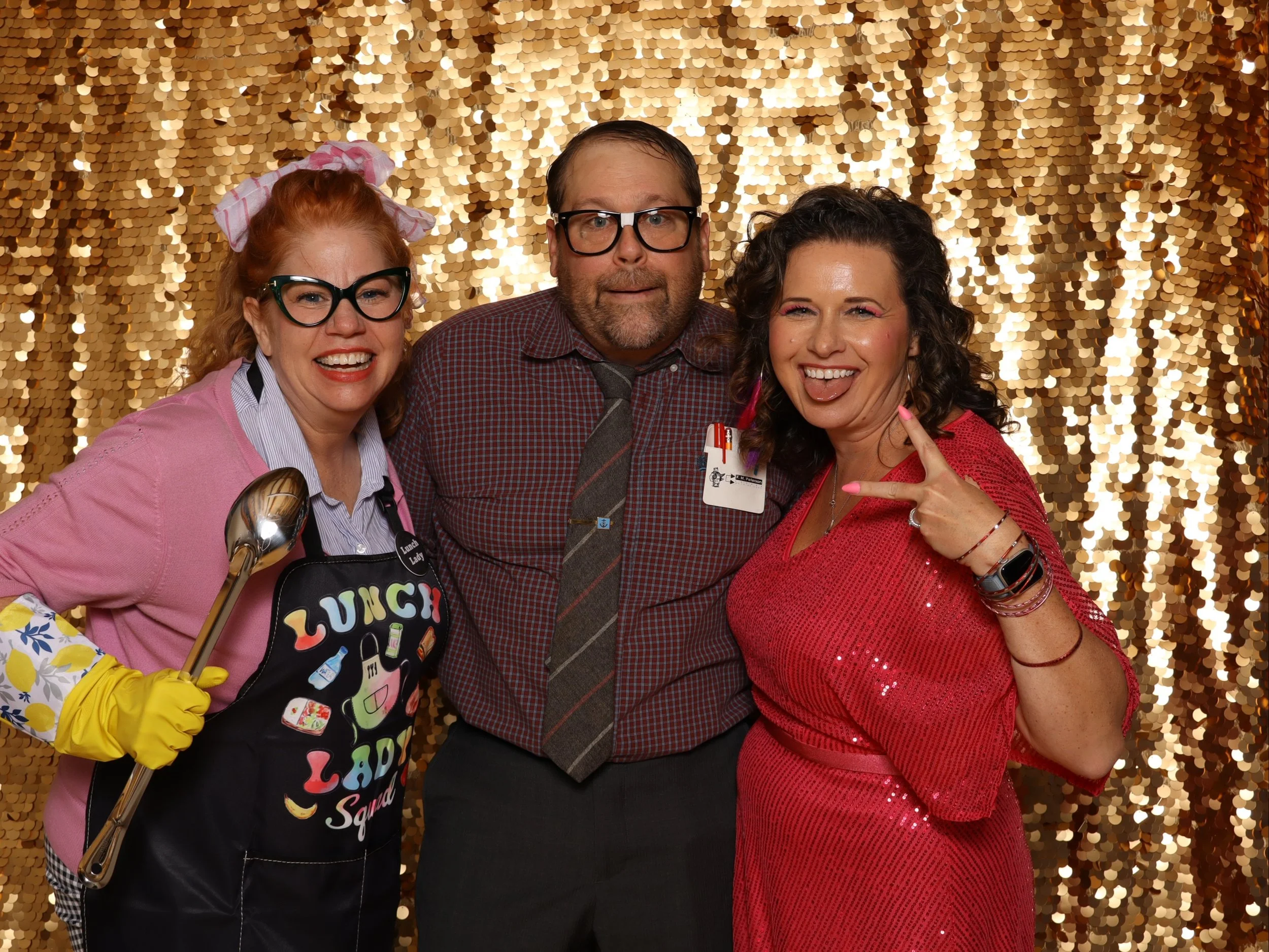 Three people posing together in front of a gold sequin backdrop, smiling and making playful gestures.  Lightning Booth Photo Booth.