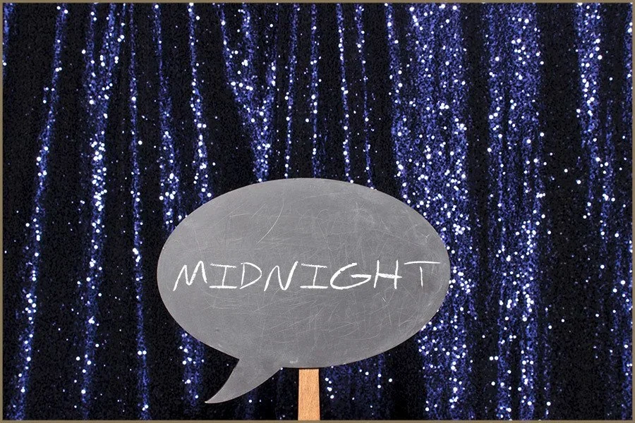 A chalkboard sign with the word "MIDNIGHT" written inside a speech bubble, set against a backdrop of glittery blue curtain.