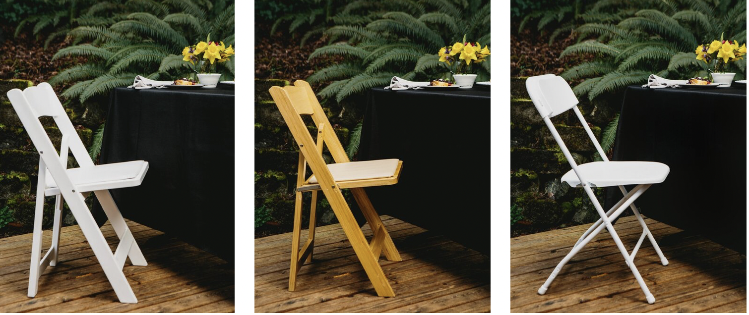 Three foldable chairs in different colors positioned in front of a table with a black tablecloth. The table has a floral arrangement with yellow flowers and a white bowl, set outdoors on a wooden deck with lush green ferns in the background.