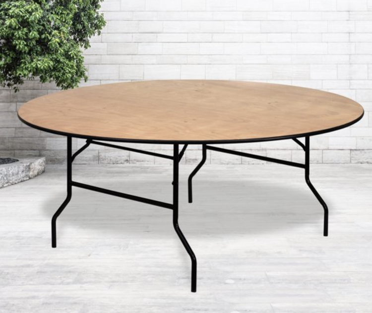Round wooden table with black metal foldable legs in a room with white brick wall and light-colored flooring.