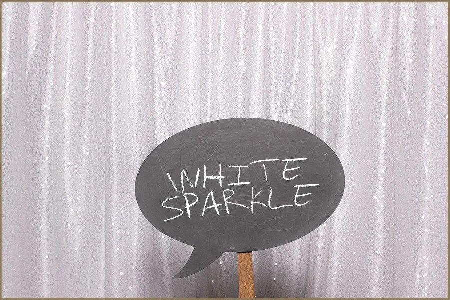 Black speech bubble sign with white chalk writing that says "White Sparkle" in front of a sparkly, silver curtain background.