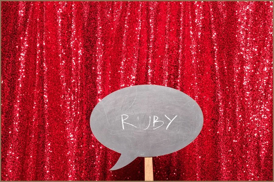 Red, sequined curtain backdrop with a chalkboard speech bubble reading 'RUBY' in front.