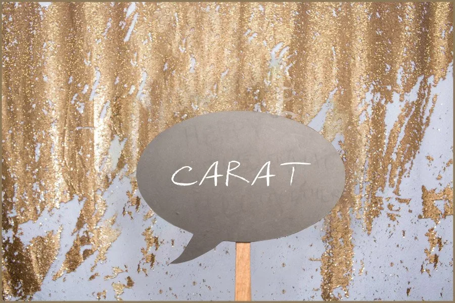 A silver speech bubble sign with the word 'CARA T' written on it, positioned against a gold glittery backdrop.