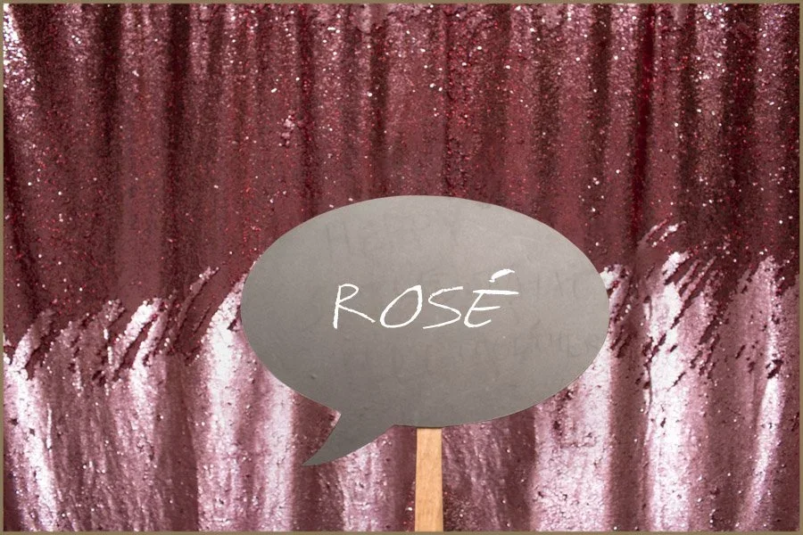 Pink and maroon glittery curtain backdrop with a speech bubble on a stick label reading 'ROSE' in white text.