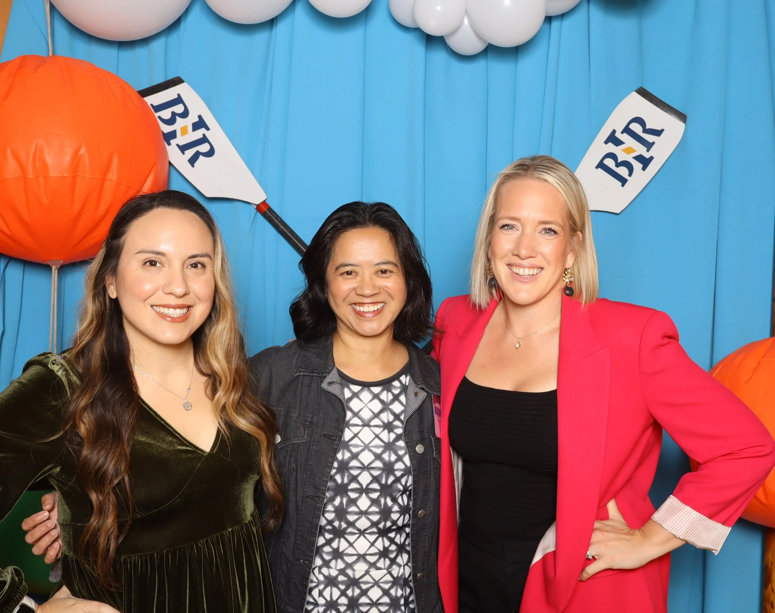 Three women standing together at a birthday celebration with blue decorations, paper lanterns, and party bunting that says "BIR" among the decorations. Lightning Booth Photo Booth.