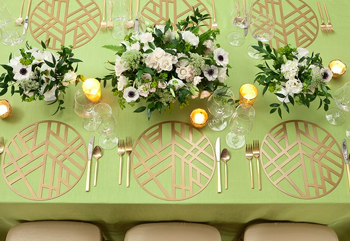 A formal dining table decorated with floral centerpieces, gold-colored placemats, glassware, and candles, set for a special event or celebration.