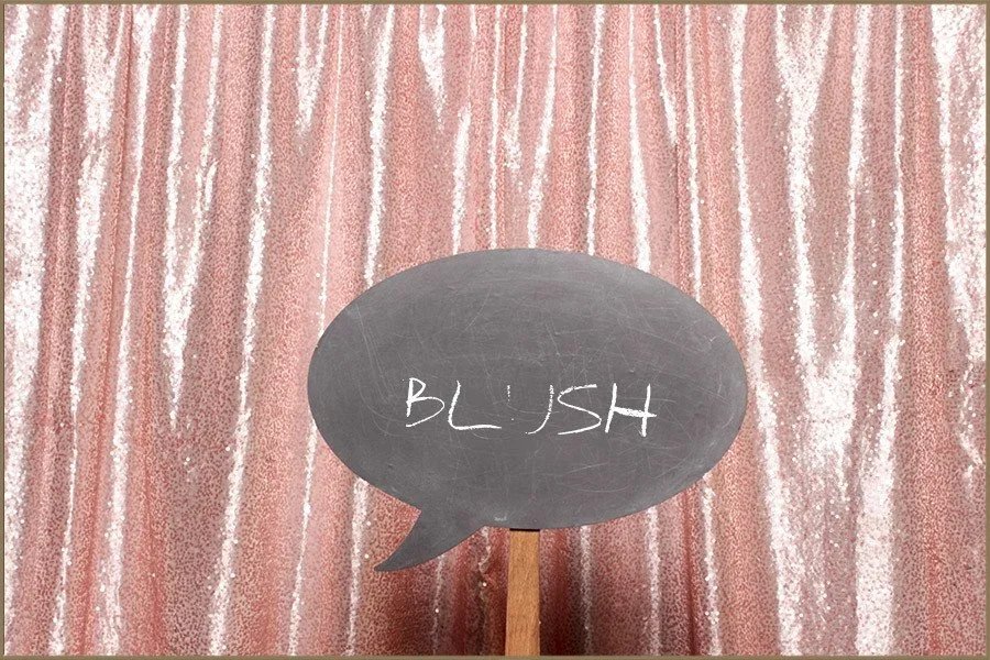 A chalkboard sign with the word 'BLUSH' written on it, positioned in front of a pink sequin curtain backdrop.