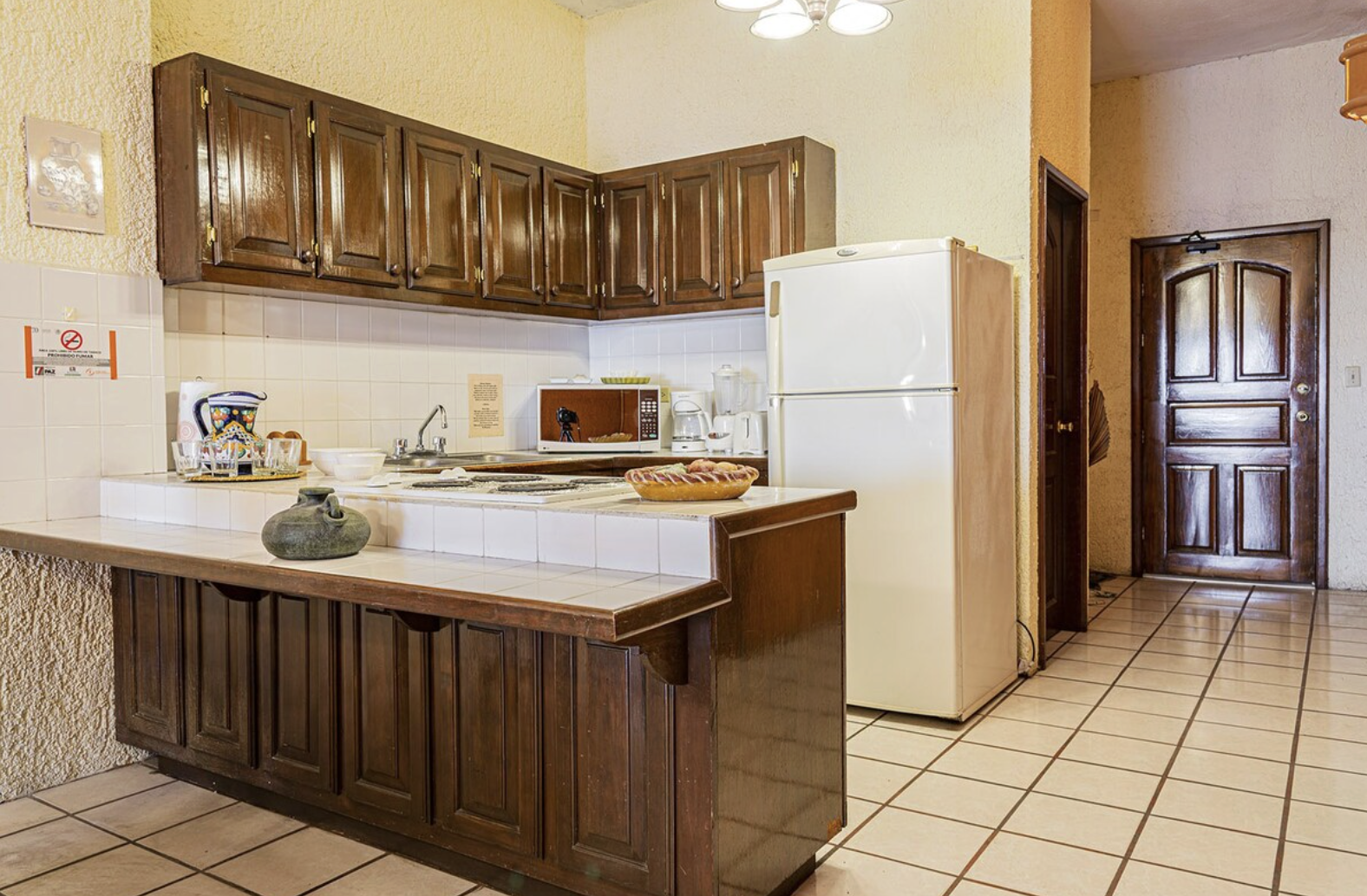 Kitchen with brown wooden cabinets, white refrigerator, microwave, coffee maker, and tiled countertops.