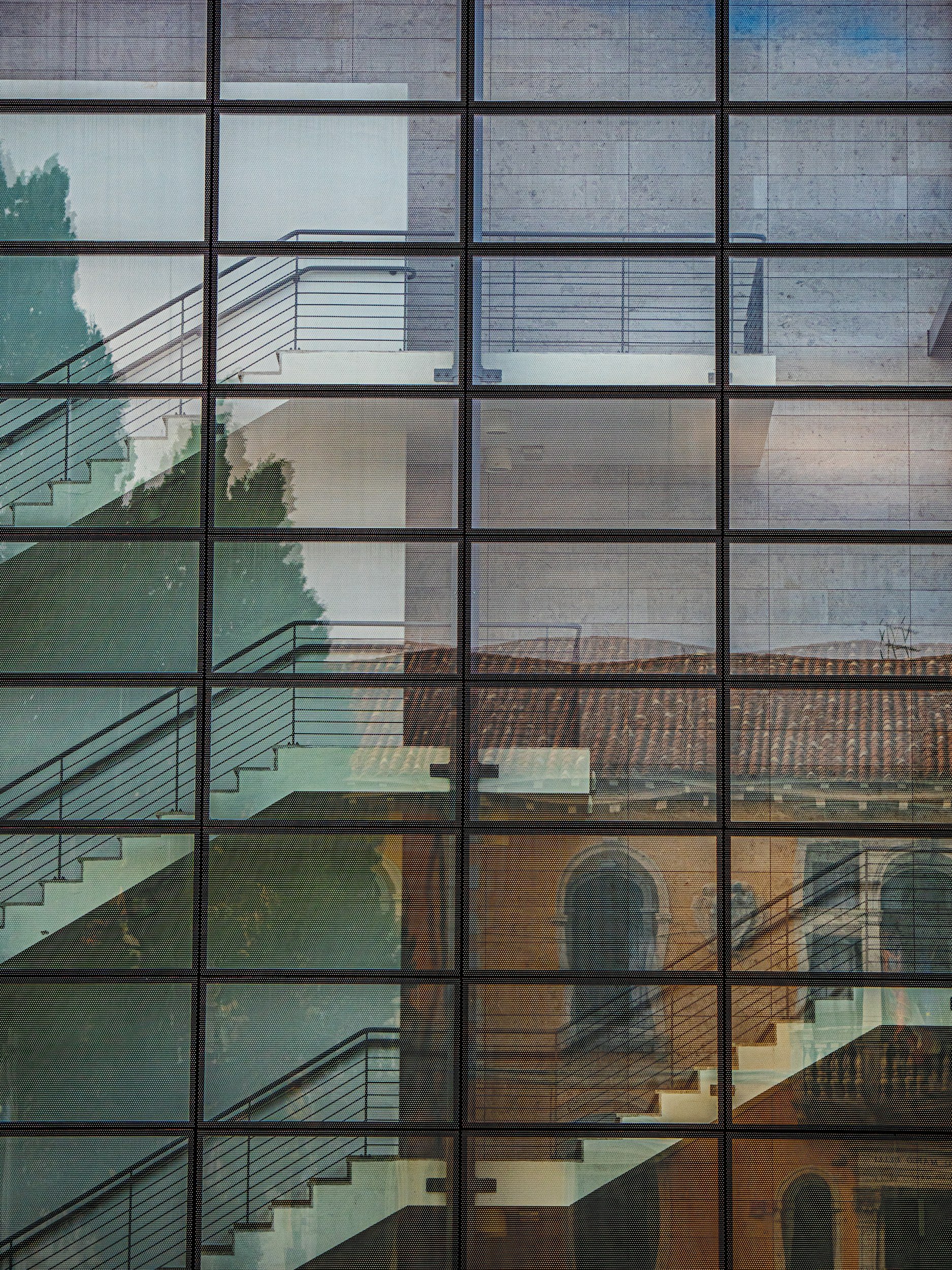 Reflection of a building with stairs and a tiled roof, seen through a glass window divided into a grid of small square panes.