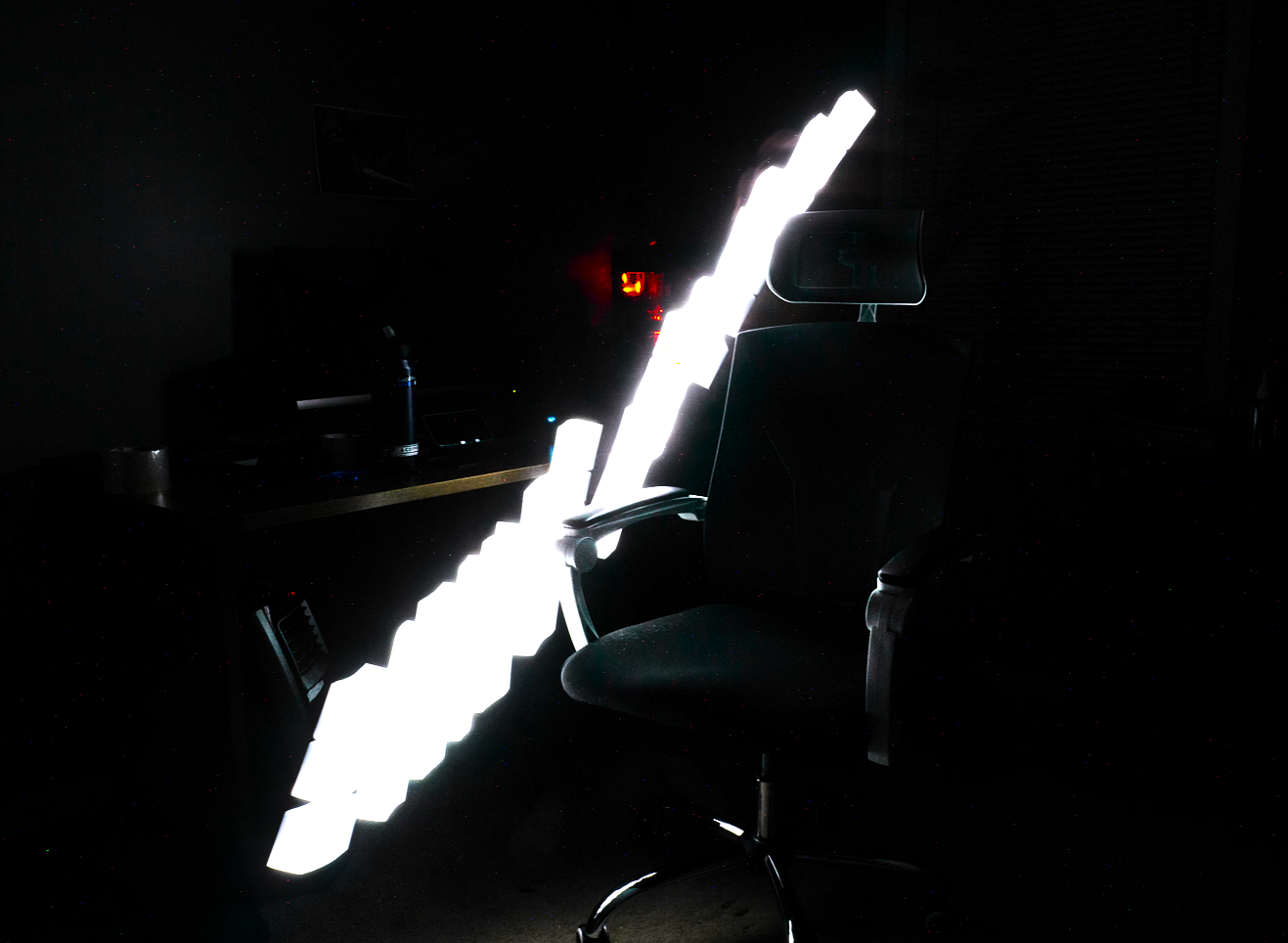 An office chair in a dark room illuminated by a bright, glowing, zigzag-shaped light source.